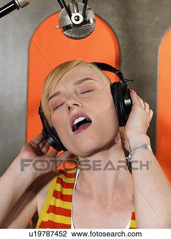 Stock Image - Young woman singing in studio, portrait. Fotosearch