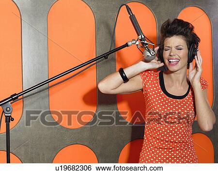 Stock Photograph - Young woman singing in studio, portrait. Fotosearch