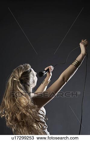 Stock Image - Young woman singing in studio. Fotosearch