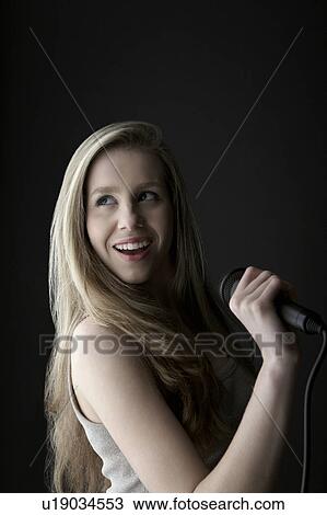 Stock Image - Young woman singing in studio. Fotosearch