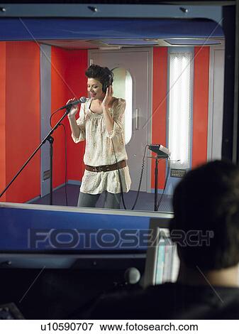 Young woman singing in studio, technician in foreground View Large Photo Image Stock Photo - Young woman singing in studio, technician in foreground. Fotosearch