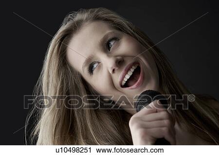 Young woman singing into microphone, close-up View Large Photo Image Stock Image - Young woman singing into microphone, close-up. Fotosearch