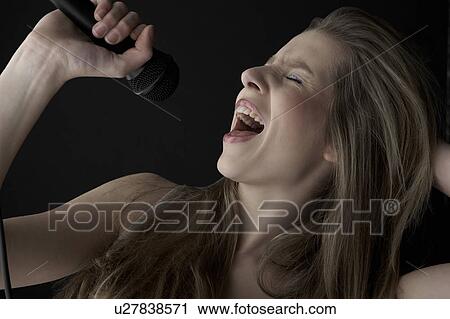 Young woman singing into microphone, close-up View Large Photo Image Stock Image - Young woman singing into microphone, close-up. Fotosearch