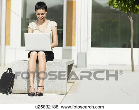 Young woman sitting in plaza courtyard using laptop View Large Photo Image Stock Photo - Young woman sitting in plaza courtyard using laptop. Fotosearch