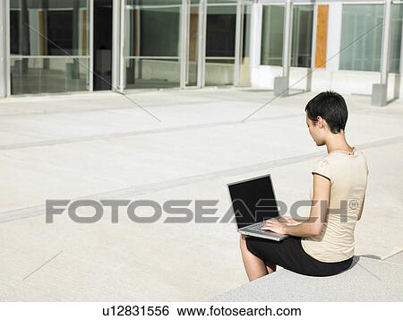 Young woman sitting in plaza courtyard using laptop View Large Photo Image Stock Photograph - Young woman sitting in plaza courtyard using laptop. Fotosearch