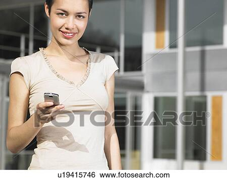 Stock Photograph - Young woman sitting in plaza sending text message, portrait. Fotosearch