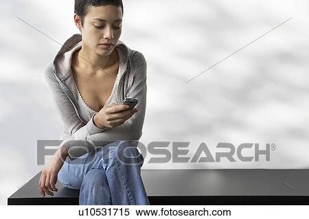 Young woman sitting indoors on bench ending text message View Large Photo Image Stock Photography - Young woman sitting indoors on bench ending text message. Fotosearch