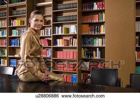 Young woman sitting on desk in library, portrait View Large Photo Image Stock Photograph - Young woman sitting on desk in library, portrait. Fotosearch