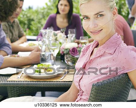 Young woman sitting with friends around patio table, socialising, eating and drinking View Large Photo Image Stock Photography - Young woman sitting with friends around patio table, socialising, eating and drinking. Fotosearch