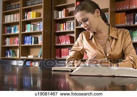 Stock Photo - Young woman writing at desk in library. Fotosearch