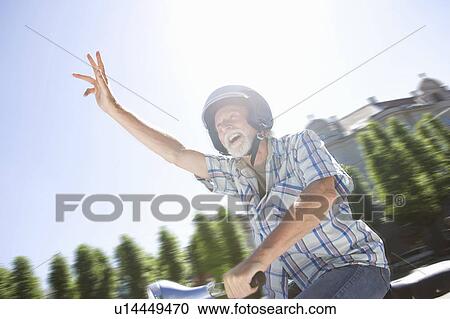 Stock Image - Man on scooter, waving. Fotosearch