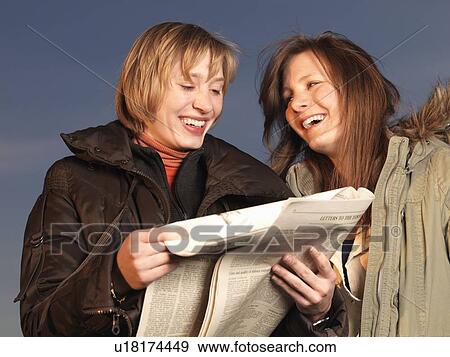 Stock Photo - Two women reading newspaper, laughing. Fotosearch