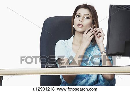 Stock Photo - Businesswoman sitting in front of a computer adjusting her earring. Fotosearch