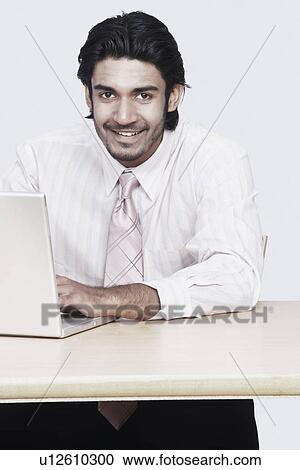 Portrait of a businessman sitting in front of a laptop View Large Photo Image Stock Image - Portrait of a businessman sitting in front of a laptop. Fotosearch