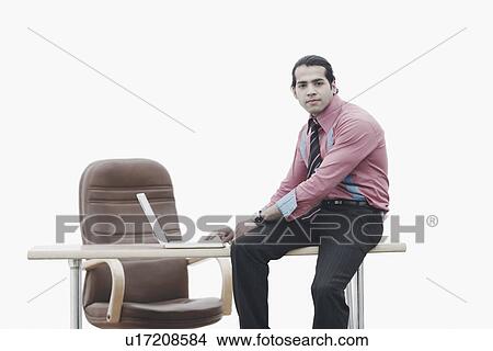 Picture - Portrait of a businessman sitting on the table working on a laptop. Fotosearch