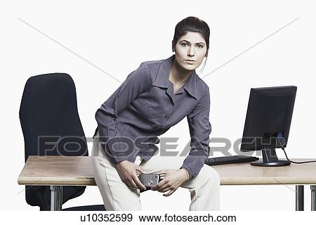 Portrait of a businesswoman sitting on a table holding a mobile phone View Large Photo Image Stock Photo - Portrait of a businesswoman sitting on a table holding a mobile phone. Fotosearch