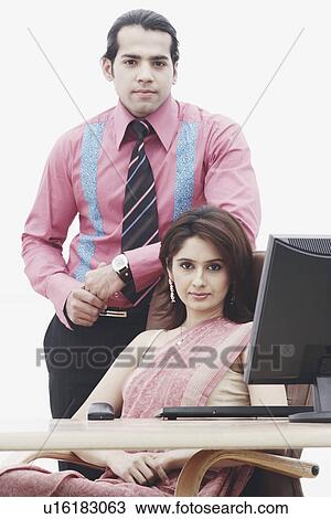 Stock Image - Portrait of a businesswoman sitting with a businessman standing beside her in an office. Fotosearch