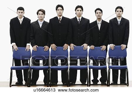 Stock Image - Portrait of a group of young men standing behind chairs. Fotosearch