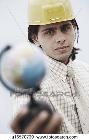 Stock Photo - Portrait of an architect wearing a hardhat holding a globe. Fotosearch