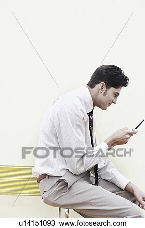 Stock Image - Side profile of a businessman holding a mobile phone. Fotosearch