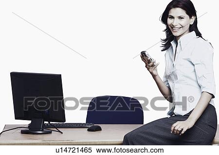 Stock Photography - Side profile of a businesswoman sitting on a table holding a mobile phone. Fotosearch