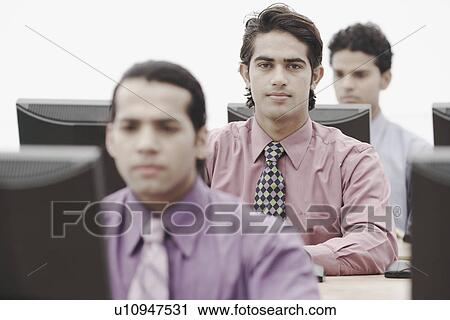 Stock Image - Three businessmen working on computers in an office. Fotosearch