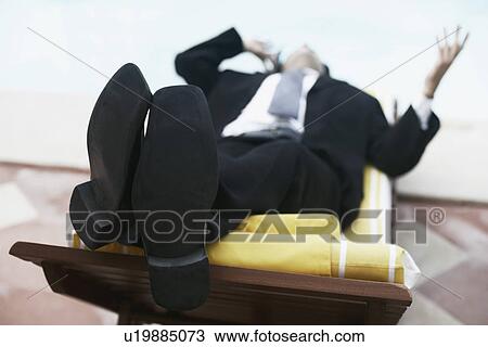 Stock Image - Close-up of a businessman lying on a lounge chair talking on a mobile phone. Fotosearch