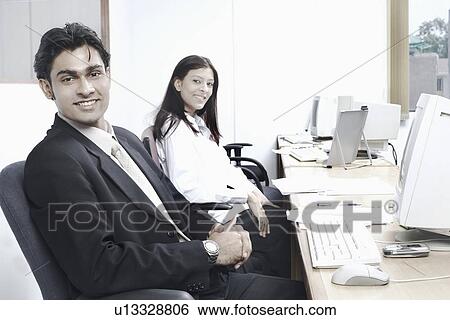 Stock Photograph - Portrait of a businessman and a businesswoman sitting in an office. Fotosearch