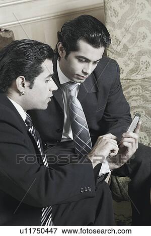 Two businessmen looking at a mobile phone View Large Photo Image Stock Photo - Two businessmen looking at a mobile phone. Fotosearch