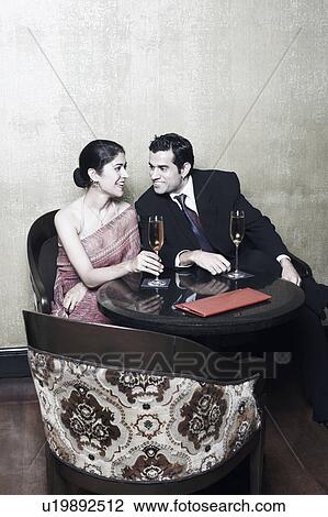 Stock Image - Businessman and a businesswoman sitting on chairs with champagne flutes. Fotosearch