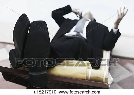 Close-up of a businessman lying on a lounge chair talking on a mobile phone View Large Photo Image Stock Image - Close-up of a businessman lying on a lounge chair talking on a mobile phone. Fotosearch