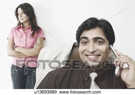 Stock Photo - Portrait of a businessman holding a mobile phone with a mid adult woman standing behind him. Fotosearch