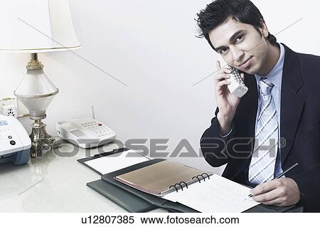 Portrait of a businessman sitting in an office talking on the telephone View Large Photo Image Stock Photography - Portrait of a businessman sitting in an office talking on the telephone. Fotosearch