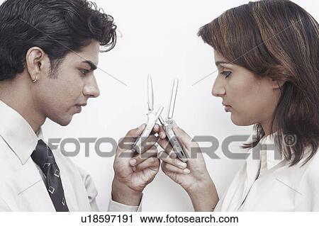 Stock Image - Side profile of a businessman and a businesswoman holding mobile phones. Fotosearch