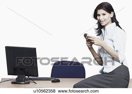 Side profile of a businesswoman sitting on a table holding a mobile phone View Large Photo Image Stock Photo - Side profile of a businesswoman sitting on a table holding a mobile phone. Fotosearch