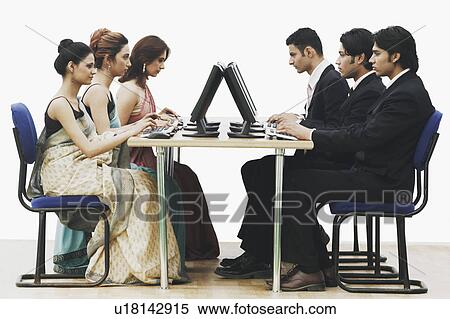 Stock Photography - Side profile of three businessmen and three businesswomen working on computers in an office. Fotosearch