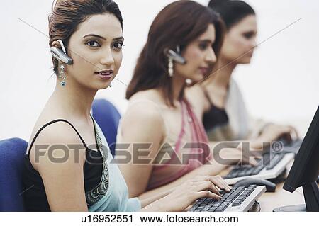 Stock Image - Side profile of three businesswomen working on computers in an office. Fotosearch