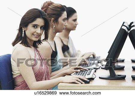 Stock Photo - Side profile of three businesswomen working on computers in an office. Fotosearch