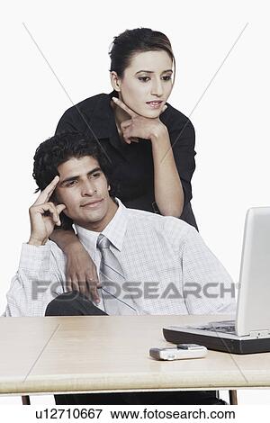 Businesswoman bending over a businessman looking at a laptop View Large Photo Image Stock Photo - Businesswoman bending over a businessman looking at a laptop. Fotosearch