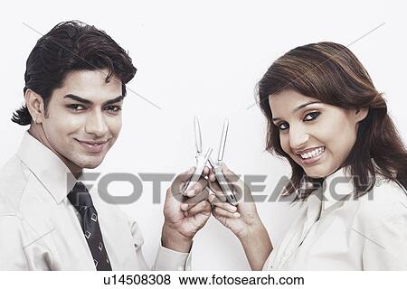 Stock Photo - Side profile of a businessman and a businesswoman holding mobile phones. Fotosearch