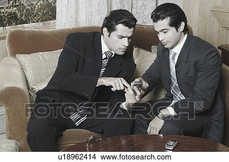 Picture - Two businessmen looking at a mobile phone. Fotosearch