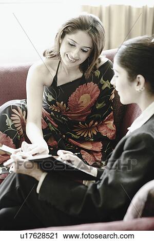 Two young women sitting on a couch discussing View Large Photo Image Stock Image - Two young women sitting on a couch discussing. Fotosearch