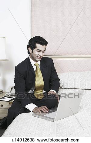 Stock Photo - Businessman sitting on the bed using a laptop. Fotosearch