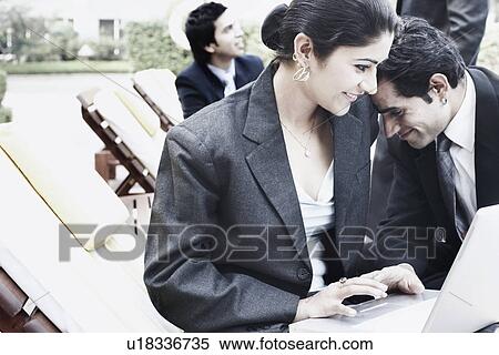 Businesswoman using a laptop with a businessman leaning on her shoulder View Large Photo Image Stock Photography - Businesswoman using a laptop with a businessman leaning on her shoulder. Fotosearch