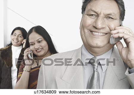 Close-up of a businessman talking on a mobile with two mature women standing behind him View Large Photo Image Stock Photo - Close-up of a businessman talking on a mobile with two mature women standing behind him. Fotosearch