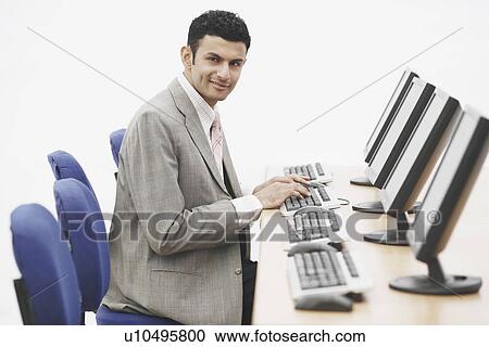 Portrait of a businessman sitting in front of a computer View Large Photo Image Stock Image - Portrait of a businessman sitting in front of a computer. Fotosearch