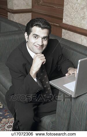 Stock Photograph - Portrait of a businessman sitting on a couch with a laptop. Fotosearch