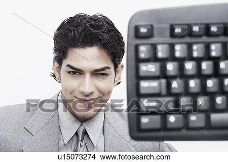Portrait of a businessman smiling behind a computer keyboard View Large Photo Image Picture - Portrait of a businessman smiling behind a computer keyboard. Fotosearch