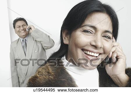 Stock Photography - Portrait of a businesswoman talking on a mobile phone with a businessman standing behind her. Fotosearch