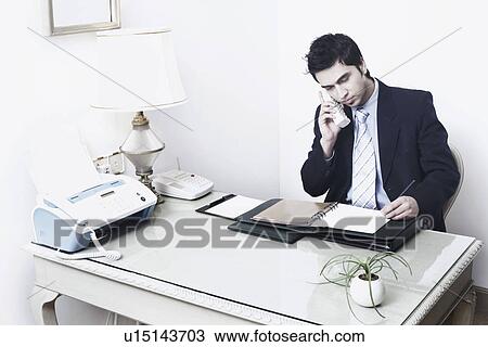 Stock Image - Businessman sitting in an office talking on the telephone. Fotosearch